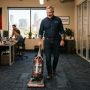 A male business owner vacuuming a commercial office floor.