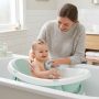 Parent gently bathing a happy infant in a baby bathtub.