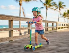 A happy child riding a scooter with an adjustable handle on a Florida sidewalk.